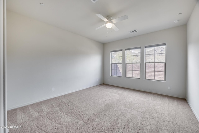 carpeted spare room with visible vents, baseboards, and a ceiling fan