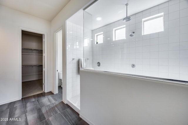bathroom with a spacious closet, a walk in shower, toilet, and baseboards