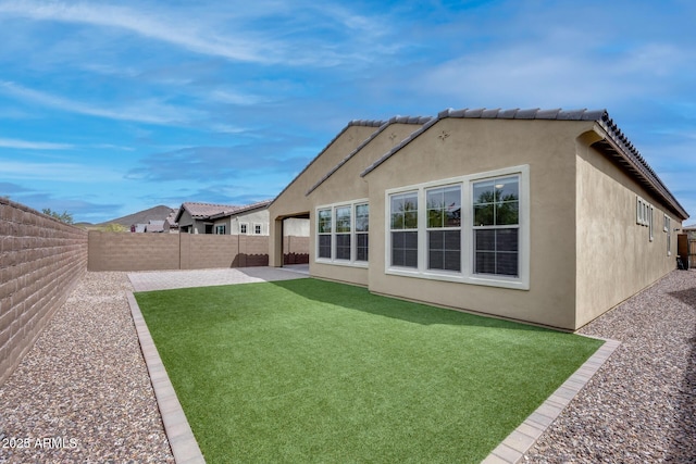 rear view of property with a fenced backyard, stucco siding, a lawn, and a patio