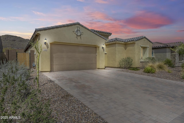 mediterranean / spanish house featuring stucco siding, decorative driveway, fence, an attached garage, and a tiled roof