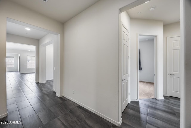 corridor featuring baseboards and dark tile patterned floors