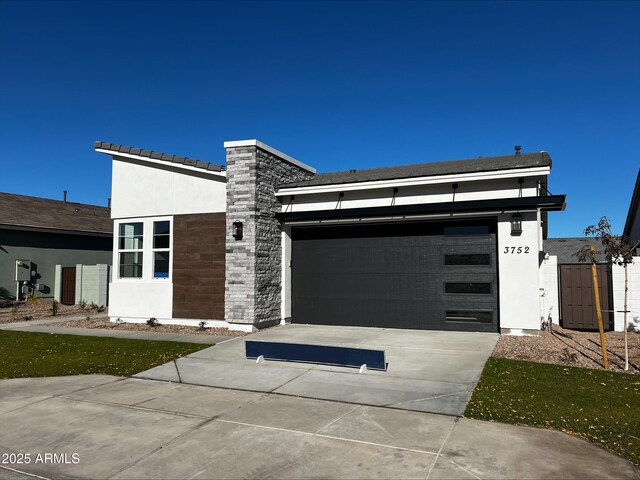 contemporary house with stucco siding, stone siding, concrete driveway, and an attached garage