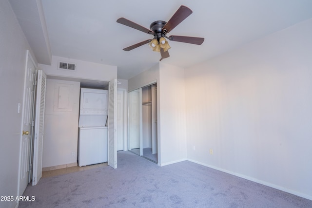 unfurnished bedroom featuring ceiling fan, stacked washing maching and dryer, and light carpet