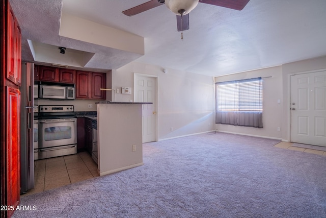 kitchen with appliances with stainless steel finishes, light carpet, kitchen peninsula, a raised ceiling, and ceiling fan