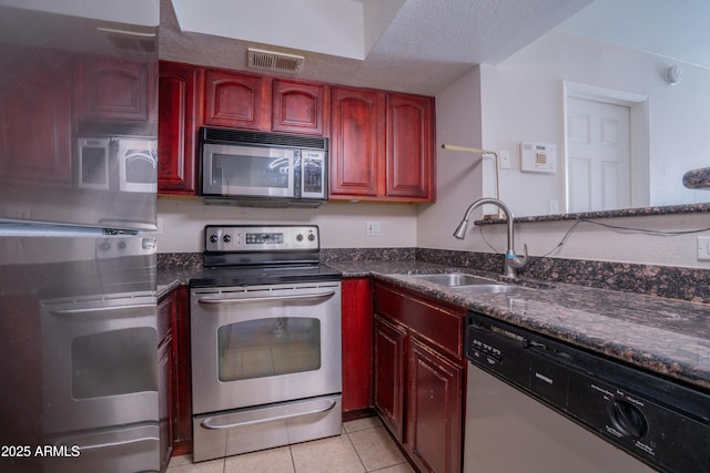 kitchen with light tile patterned floors, appliances with stainless steel finishes, dark stone counters, a textured ceiling, and sink