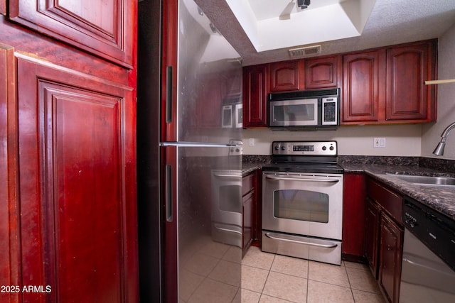 kitchen featuring sink, light tile patterned floors, stainless steel appliances, and dark stone counters