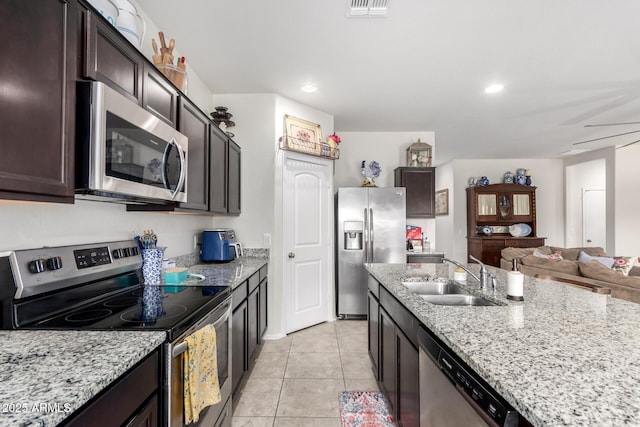 kitchen with light tile patterned flooring, appliances with stainless steel finishes, sink, light stone counters, and dark brown cabinetry