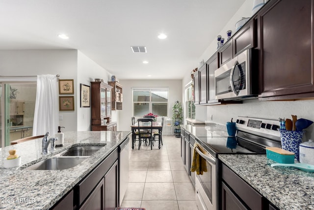 kitchen with dark brown cabinetry, sink, light tile patterned floors, stainless steel appliances, and light stone countertops