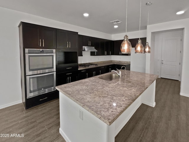 kitchen with an island with sink, appliances with stainless steel finishes, dark hardwood / wood-style floors, and pendant lighting