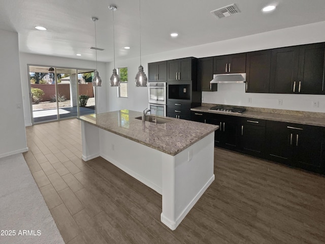 kitchen featuring decorative light fixtures, dark hardwood / wood-style flooring, a kitchen island with sink, gas cooktop, and light stone countertops