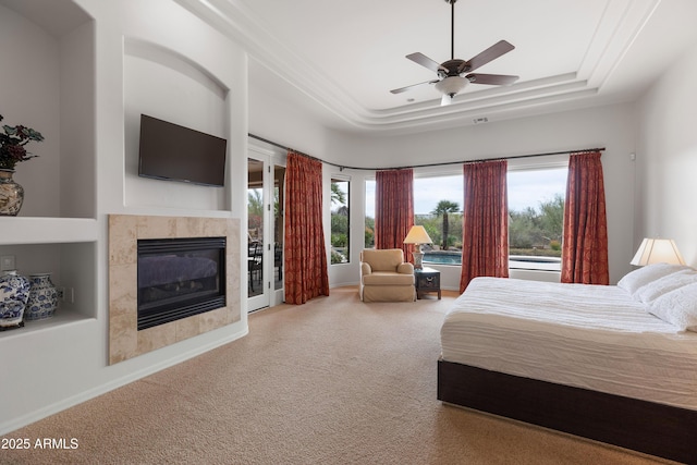 bedroom with carpet, a tray ceiling, ceiling fan, access to exterior, and a tiled fireplace