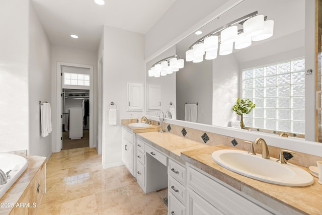 full bathroom featuring double vanity, a spacious closet, tiled tub, and a sink