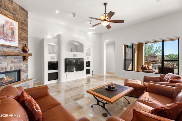 living area with ceiling fan, baseboards, built in features, a fireplace, and arched walkways