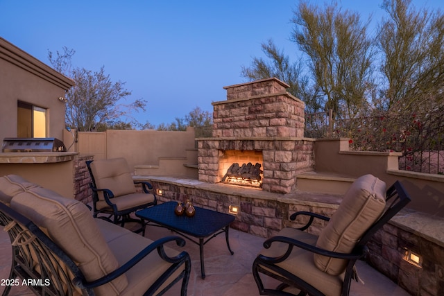 patio terrace at dusk featuring an outdoor stone fireplace and fence