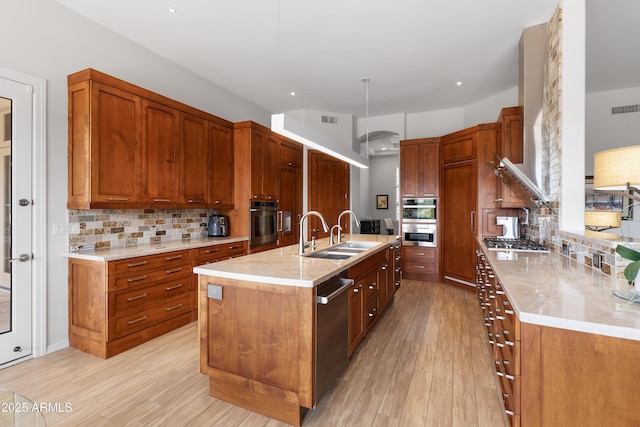 kitchen featuring visible vents, a kitchen island with sink, light wood finished floors, and a sink