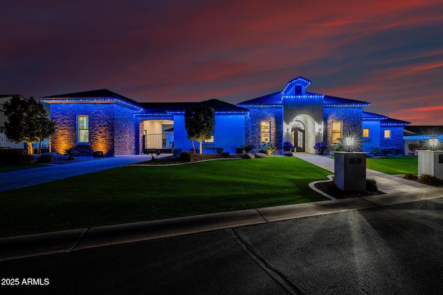 mediterranean / spanish-style home with stucco siding, stone siding, and a front lawn