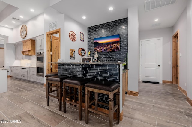 bar with a dry bar, recessed lighting, visible vents, and backsplash