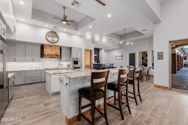 kitchen featuring visible vents, gray cabinets, a large island with sink, and a raised ceiling