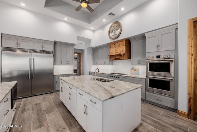 kitchen featuring visible vents, gray cabinetry, built in appliances, a ceiling fan, and a sink