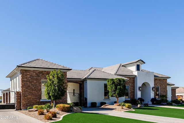 view of front of property featuring stucco siding, stone siding, a front lawn, and a tiled roof