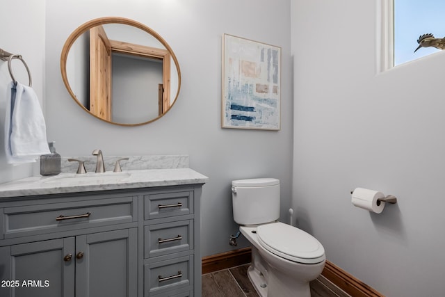 half bath featuring baseboards, toilet, wood finished floors, and vanity