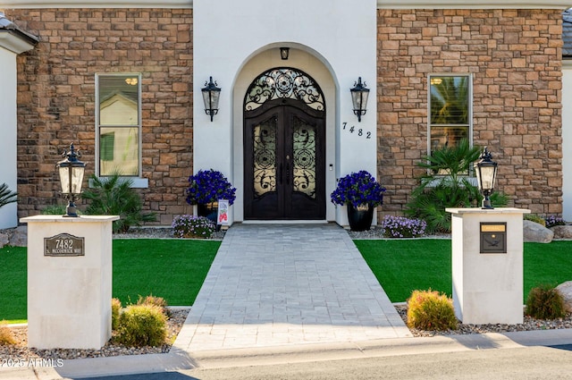 property entrance with a yard, french doors, stone siding, and stucco siding