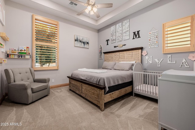 bedroom with visible vents, baseboards, ceiling fan, light colored carpet, and a tray ceiling