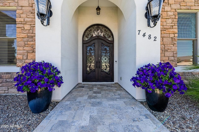 entrance to property featuring french doors, stone siding, and stucco siding