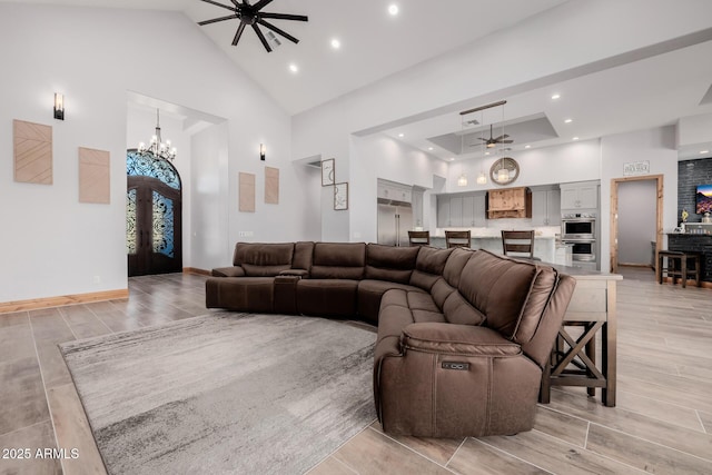 living area with baseboards, high vaulted ceiling, wood tiled floor, and ceiling fan with notable chandelier