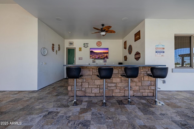 bar with a community bar, ceiling fan, and stone finish floor