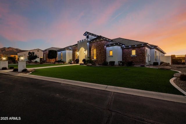 view of front facade featuring a front lawn, a tiled roof, stone siding, and stucco siding