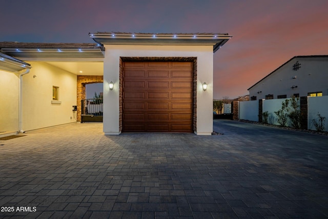 garage at dusk with decorative driveway and fence