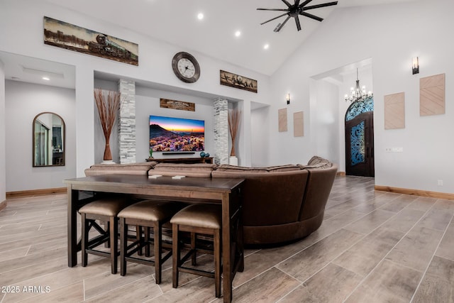 living room featuring high vaulted ceiling, ceiling fan with notable chandelier, recessed lighting, baseboards, and wood tiled floor