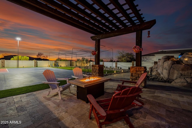 patio terrace at dusk featuring fence, a fire pit, and a pergola