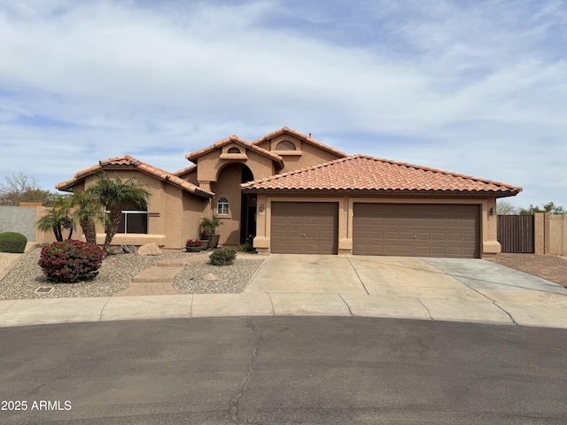 mediterranean / spanish home featuring a garage, driveway, a tiled roof, fence, and stucco siding