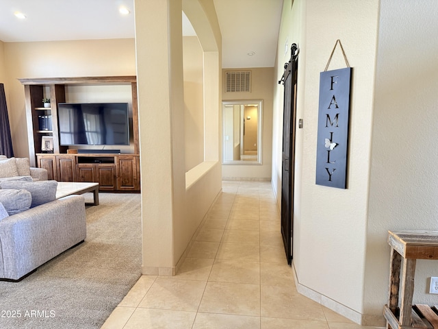 corridor with light tile patterned floors, arched walkways, a barn door, visible vents, and baseboards