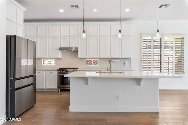 kitchen featuring white cabinets, stainless steel appliances, hanging light fixtures, and an island with sink