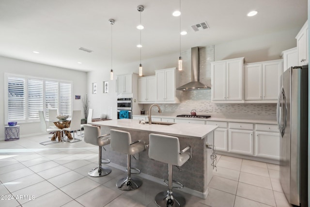 kitchen with a kitchen island with sink, wall chimney range hood, sink, decorative light fixtures, and stainless steel appliances