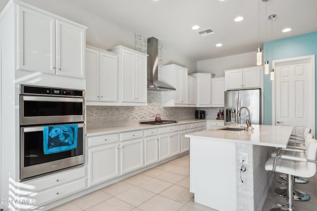 kitchen featuring white cabinets, stainless steel appliances, hanging light fixtures, and wall chimney exhaust hood