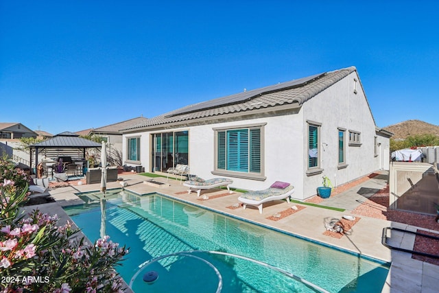 back of property with solar panels, a fenced in pool, a patio area, and a gazebo