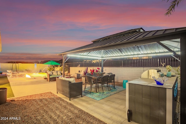 patio terrace at dusk with an outdoor kitchen, a grill, and an outdoor living space with a fire pit