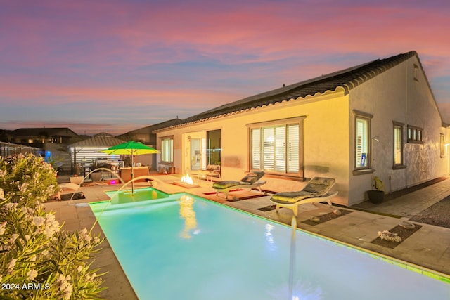 pool at dusk with pool water feature and a patio