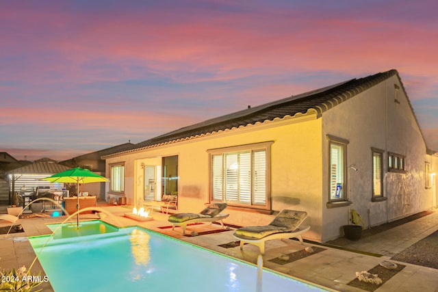 back house at dusk featuring pool water feature, a patio area, and an outdoor fire pit