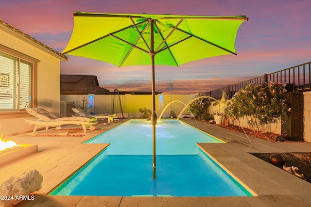 pool at dusk with pool water feature, a patio, and an outdoor fire pit