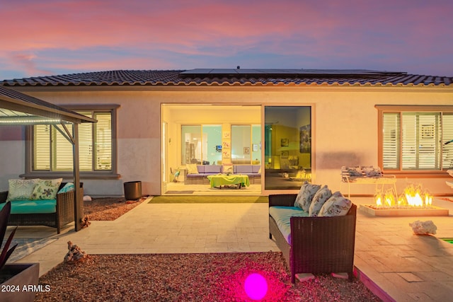 back house at dusk featuring a patio and an outdoor living space with a fire pit