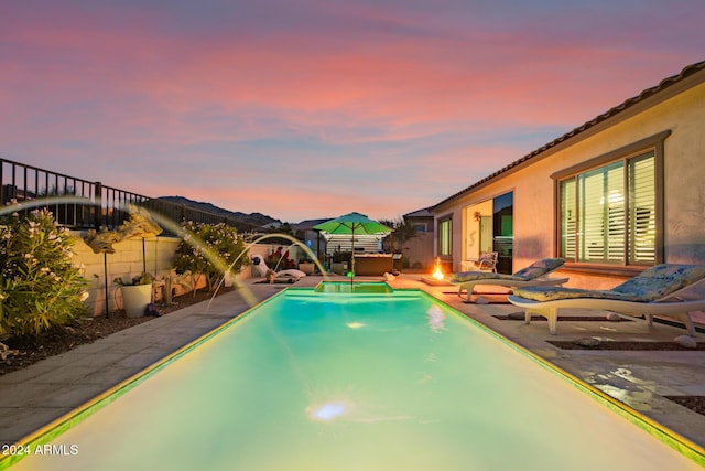 pool at dusk featuring pool water feature, a patio area, and an outdoor fire pit