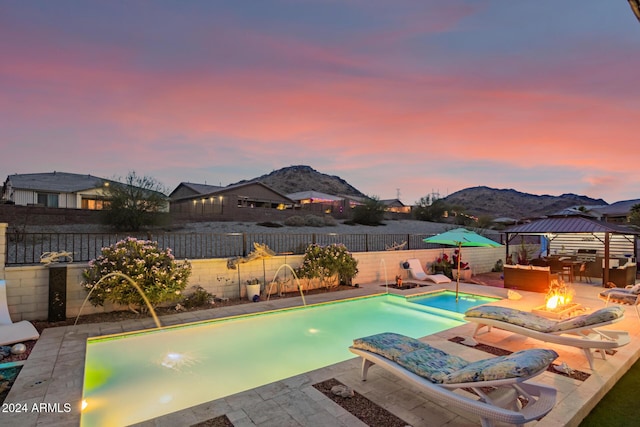 pool at dusk with a gazebo, pool water feature, a mountain view, and an outdoor fire pit