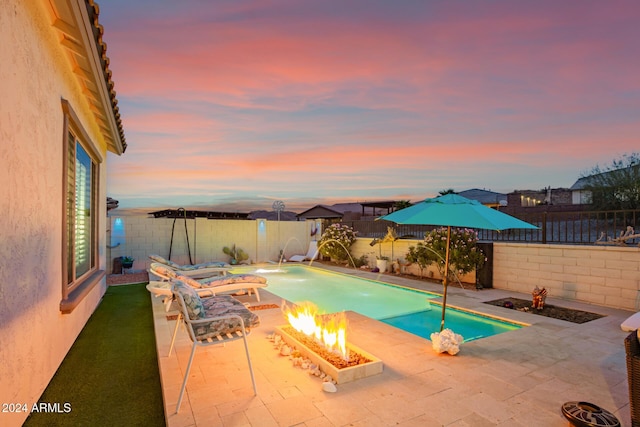 pool at dusk with pool water feature and a fire pit