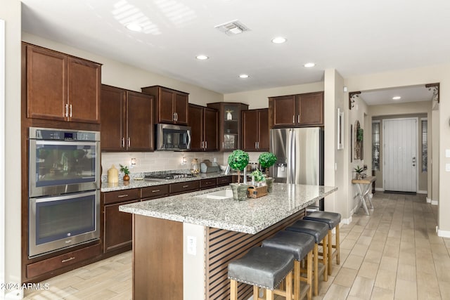 kitchen with light stone counters, a center island, sink, a kitchen bar, and stainless steel appliances