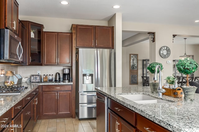 kitchen featuring pendant lighting, sink, stainless steel appliances, backsplash, and light stone countertops